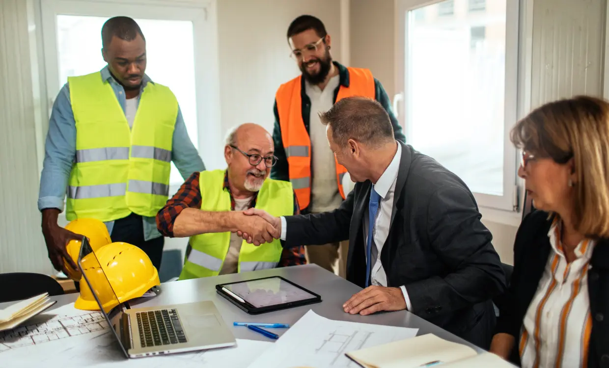 Construction meeting with handshake and safety gear.