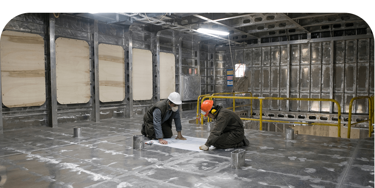 Workers reviewing plans in metal interior.