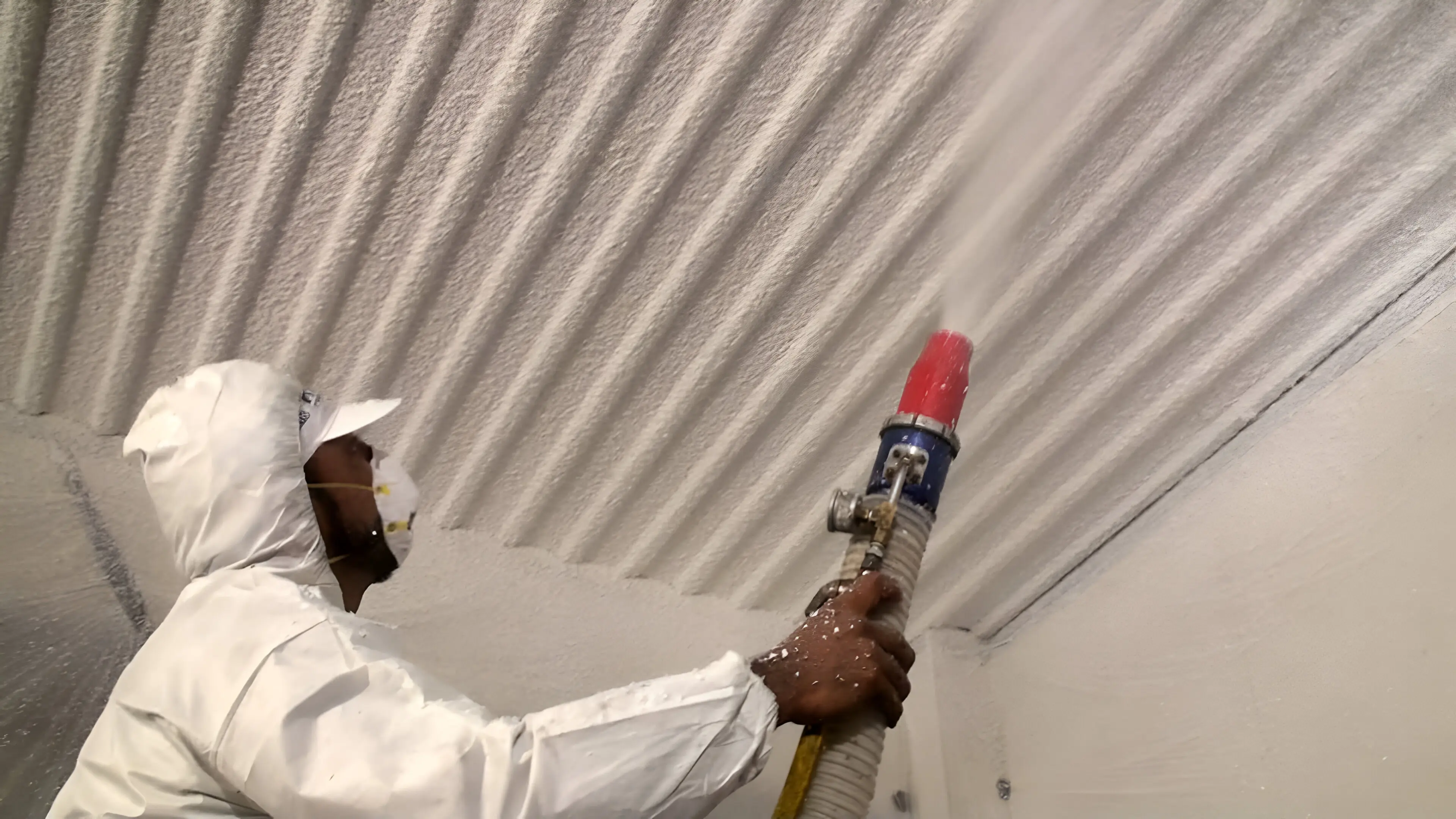 Worker spraying insulation on corrugated ceiling.