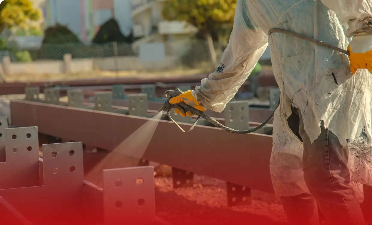 Worker spray painting metal beams outdoors.