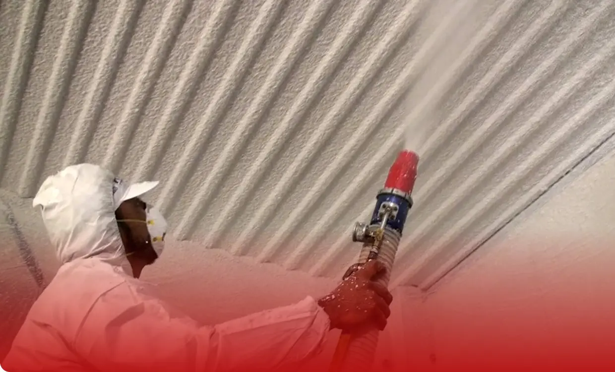 Worker spraying insulation on corrugated ceiling.