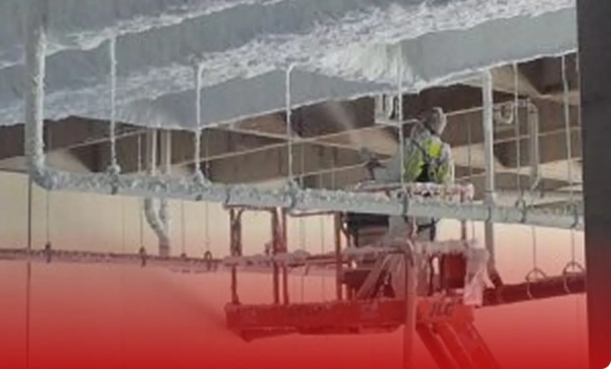 Worker on lift applying insulation to ceiling.